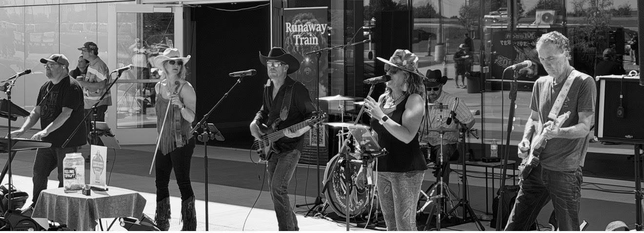 Runaway Train playing live — keys, vocals, bass, drums and guitars lined up in front of the band banner